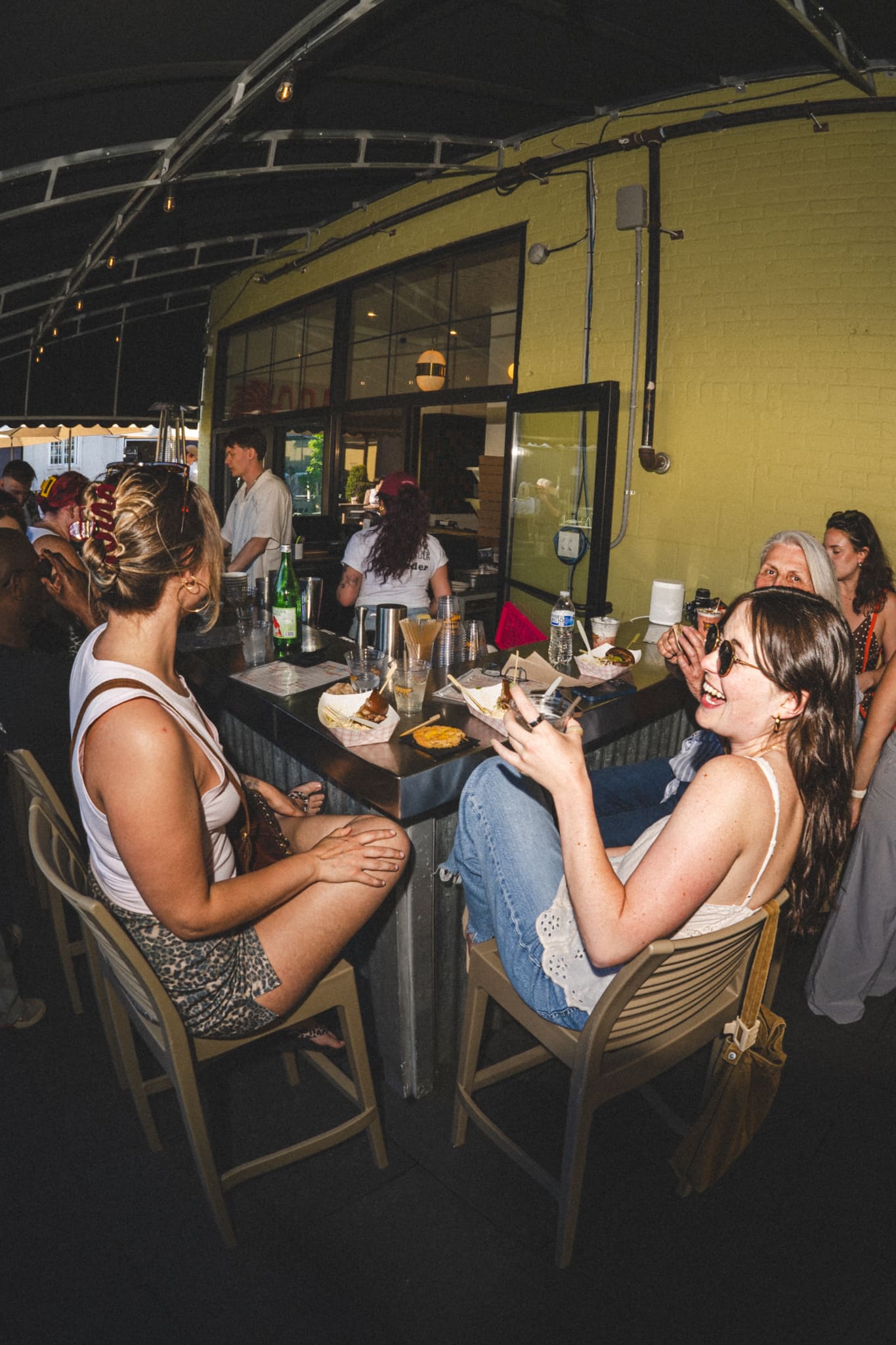 Friends laughing at the Coop bar in the evening, plates of food on the counter